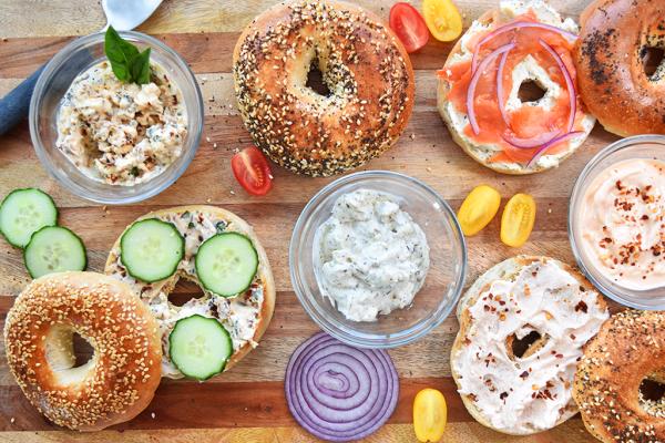 Assortment of bagels with homemade cream cheese varieties and toppings on a wooden board