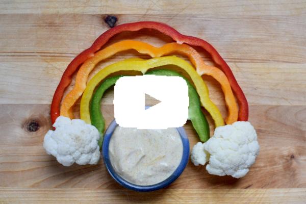 Rainbow made of colorful peppers and cauliflower clouds with a bowl of dip