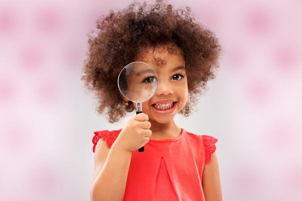 Child holding a magnifying glass. Thumbnail image for the early childhood activity Exploring Food with the 5 Senses. 