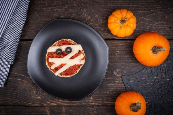 Pizza mummy made with english muffin on a plate with pumpkins beside it