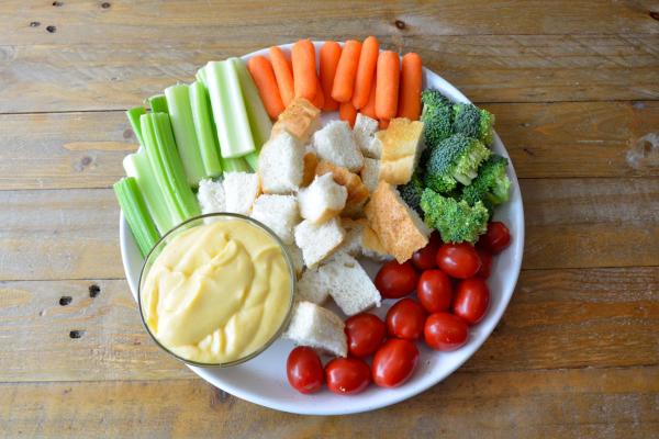 Cheese sauce in a bowl served with bread and raw veggies on a white plate
