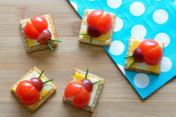 Square cracker and cheese with sliced tomatoes and grapes made to look like a ladybug