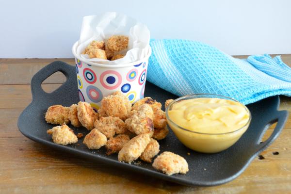 Popcorn chicken served on a black platter with cheese sauce