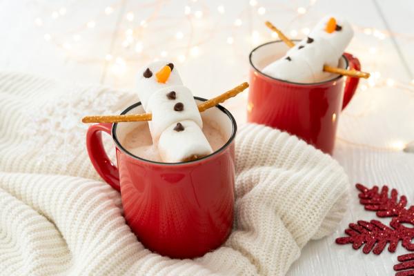 Marshmallow snowman laying on top of a mug of hot chocolate