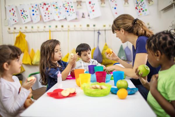 teacher sitting with children at a table eating