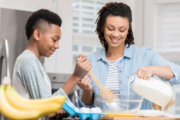 Mother and son collaboratively baking cookies, with the mother pouring milk while the son stirs the mixture using a wooden spoon