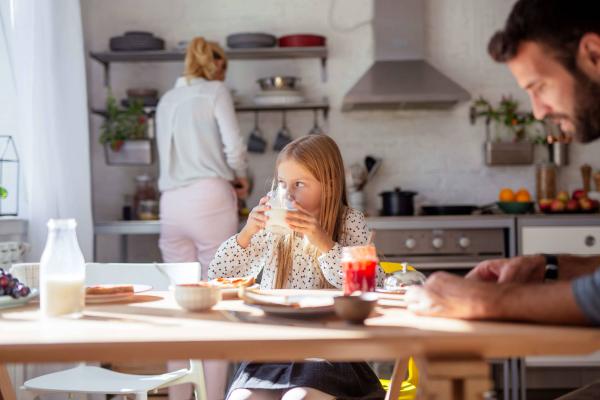 Family prepares breakfast as daughter enjoys milk, highlighting the role of dairy in diet