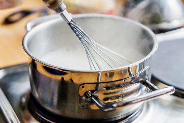 A pot on the stove with milk being heated and stirred with a whisk, perfect for making hot chocolate.