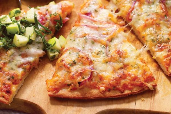 A freshly baked slice of pizza with melted Swiss cheese, topped with a zesty green salad, served on a wooden board for a tasty meal.
