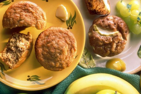 Warm banana muffins on a yellow plate with butter, surrounded by fresh fruit