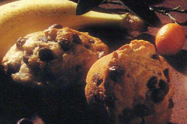 Freshly baked chocolate chip muffins on a cooling rack with scattered chocolate chips around