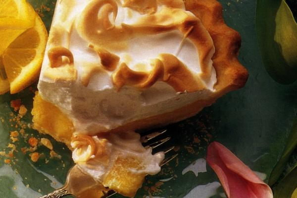 Close-up of a slice of lemon meringue pie with golden brown peaks on a green plate