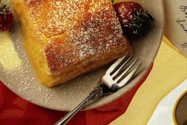 Close-up view of a tangy lemon pudding cake served on a plate with a fork, accompanied by a fresh berry, illustrating the perfect dessert for lemon lovers