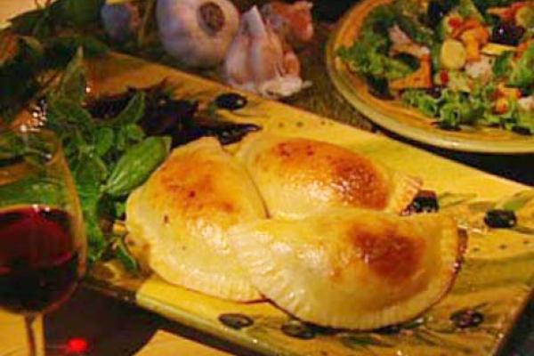 Golden-brown calzones stuffed with ricotta cheese on a ceramic plate, served with a side salad and a glass of red wine, creating an inviting Italian meal.