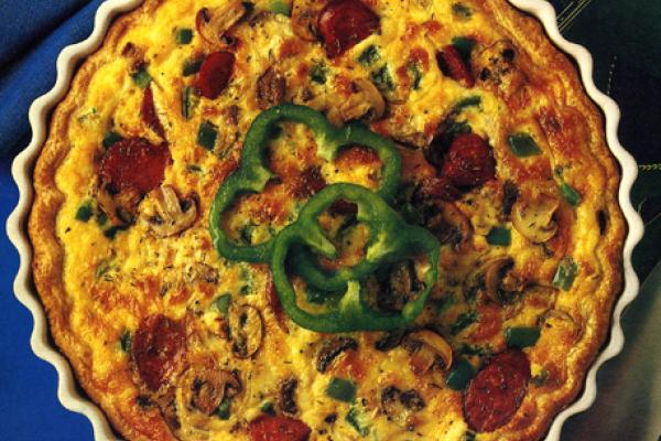 A golden-brown pizza quiche in a fluted pie dish, topped with slices of pepperoni, mushrooms, and a green bell pepper ring, ready to be served.