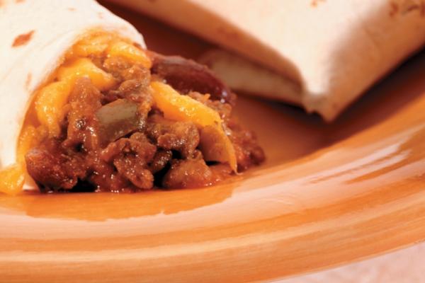 A close-up of a Sloppy Joe burrito cut in half, revealing the savory filling of ground beef, cheddar cheese, and peppers, on a ceramic plate with orange swirls