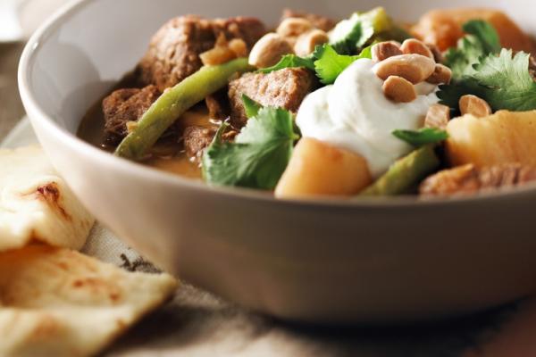 Bowl of beef curry topped with yogurt and served with naan