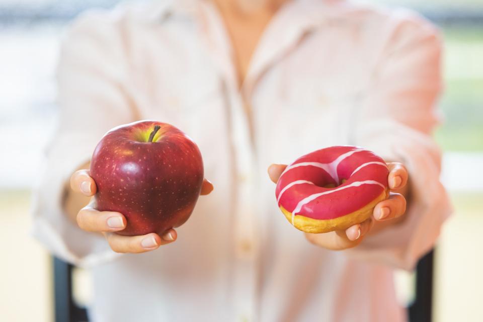 woman holding an apple in one hand and a doughnut in the other
