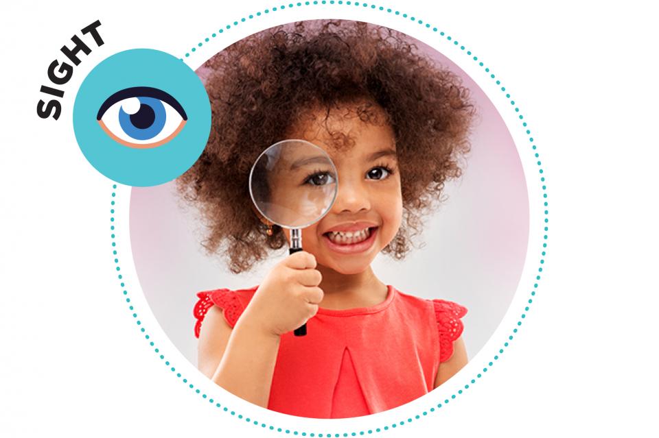 Little girl holding a magnifying glass to her eye.