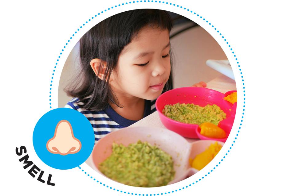 Little girl smelling food at the table.