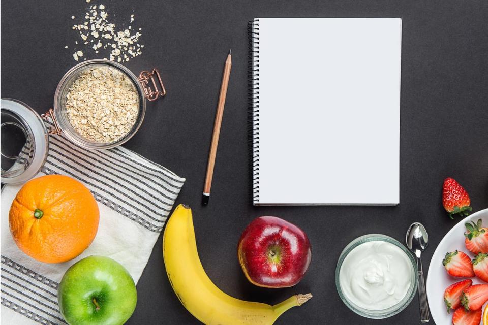 Overhead shot of booklet and pencil surrounded with fruits, oats and yogourt 