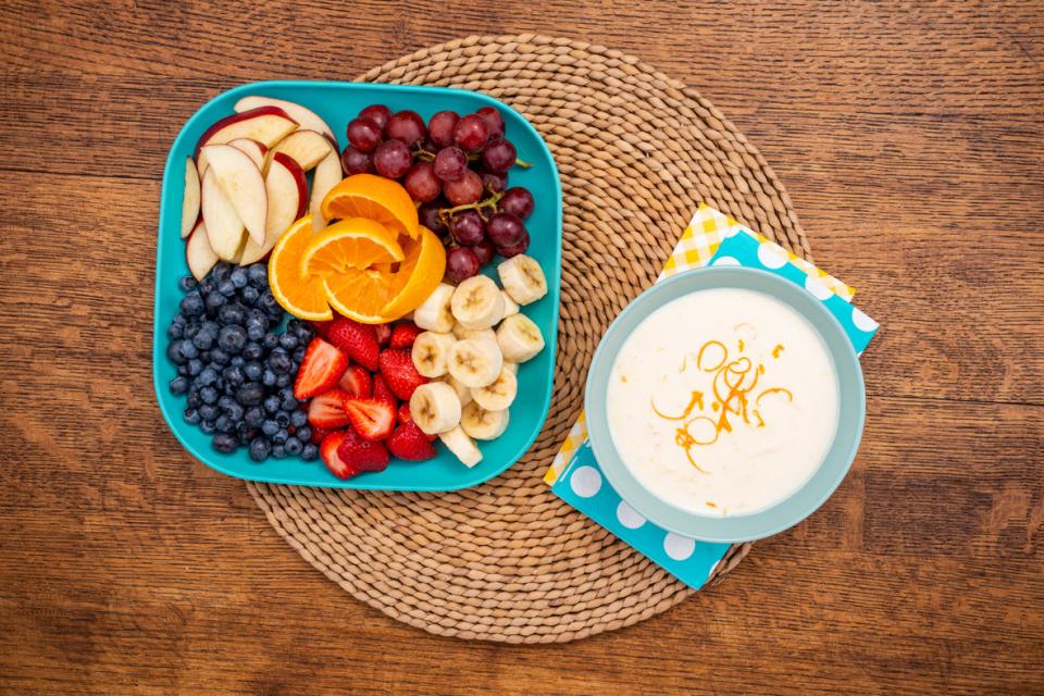 Orange fruit dip in a bowl with a platter of fruit on a table
