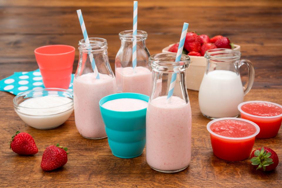 Strawberry smoothie in glass bottles and small cups with straws on a table with fresh strawberries and fruit sauce