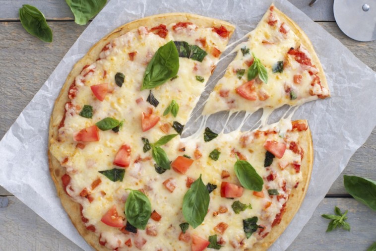 Freshly baked Italian pizza with tomato, basil, and melted cheese being sliced on parchment paper