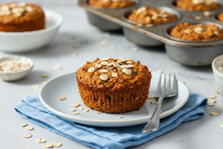 Oatmeal carrot muffin on plate with scattered oats.