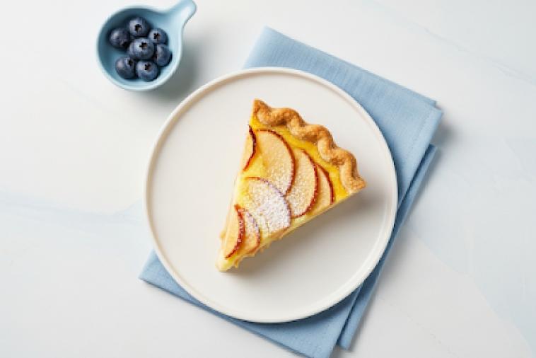 Top down image of a slice of apple custard pie, topped with icing sugar