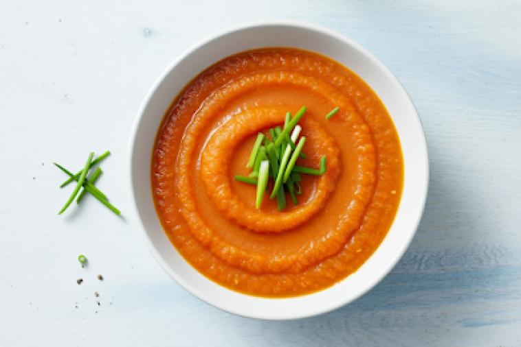 Top down image of orange leek soup, topped with leeks