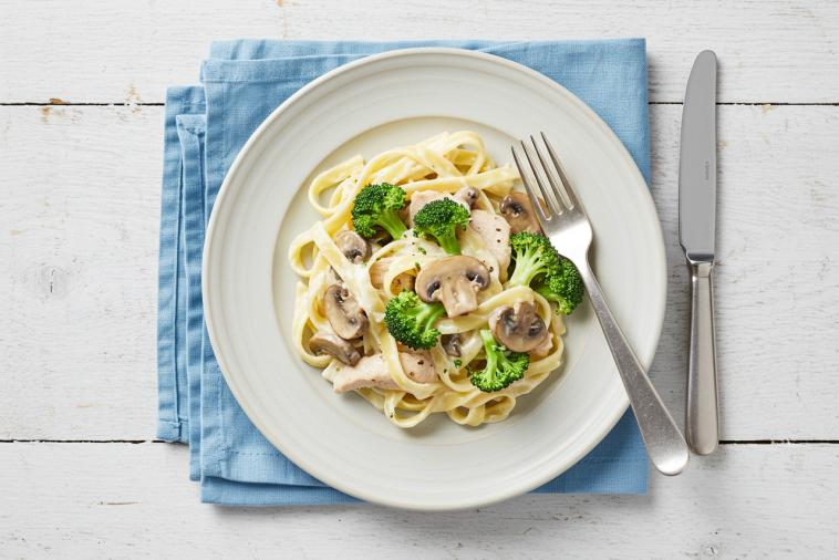 Top-down image of fettuccine alfredo with chicken, mushrooms, and broccoli on a plate