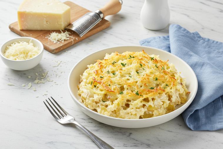 Grated potato and cheese casserole in a baking dish with parmesan cheese in the background