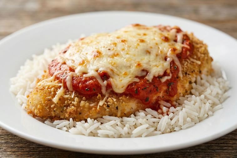 Succulent Chicken Parmesan with a crispy golden coating, smothered in tomato sauce, atop a bed of wild rice blend