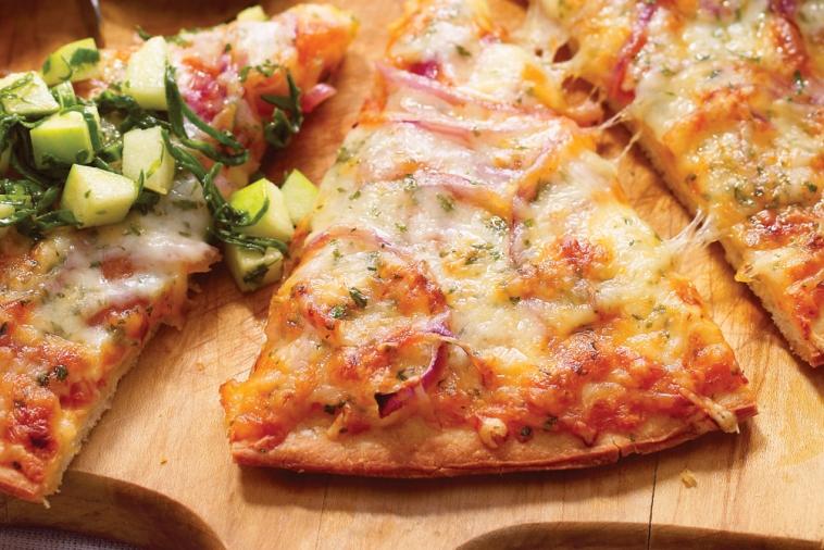 A freshly baked slice of pizza with melted Swiss cheese, topped with a zesty green salad, served on a wooden board for a tasty meal.