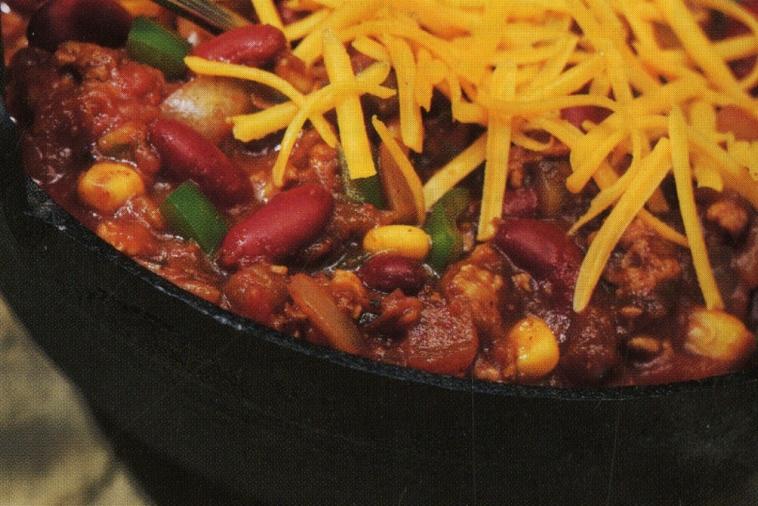 Steaming pot of chili with shredded cheddar cheese, kidney beans, corn, and green bell pepper
