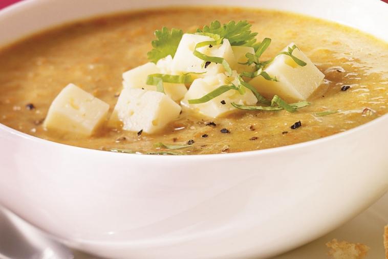 A bowl of curried lentil soup topped with diced Havarti cheese and fresh cilantro, a warm and comforting dish with a hint of spice.