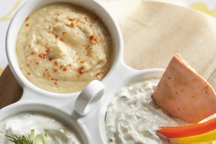 hummus Creamy hummus topped with paprika in a white serving dish with pita and tzatziki sauce on the side
