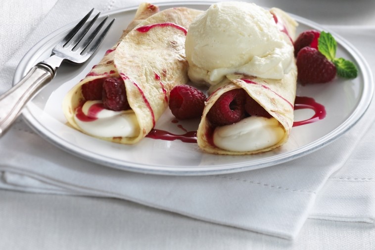 Elegant crepes filled with fresh raspberries and cream, drizzled with raspberry sauce and served with a scoop of vanilla ice cream on a white plate, ready to be enjoyed.