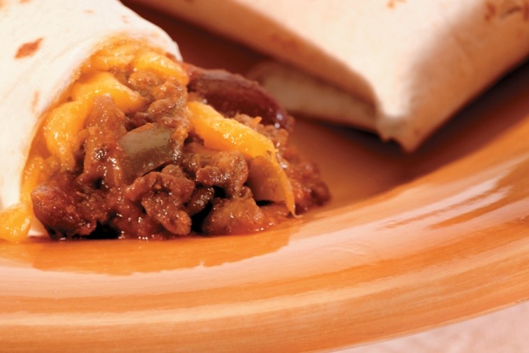 sloppy joe burritos A close-up of a Sloppy Joe burrito cut in half, revealing the savory filling of ground beef, cheddar cheese, and peppers, on a ceramic plate with orange swirls