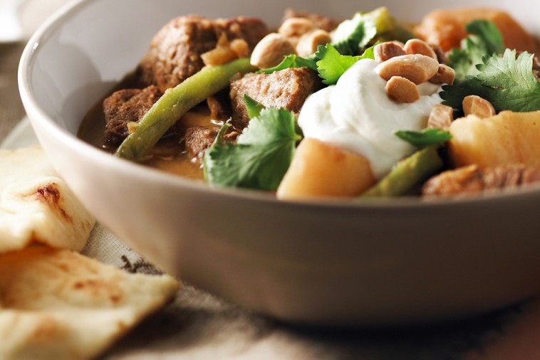 Bowl of beef curry topped with yogurt and served with naan