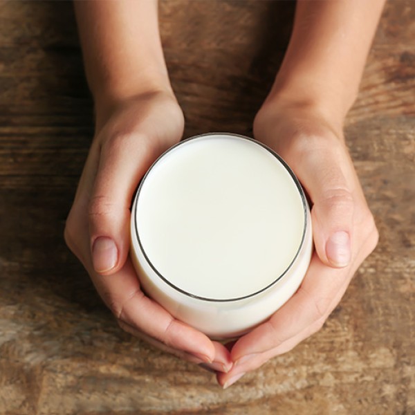 An overhead view of two hands holding a glass full of milk on a wooden table.